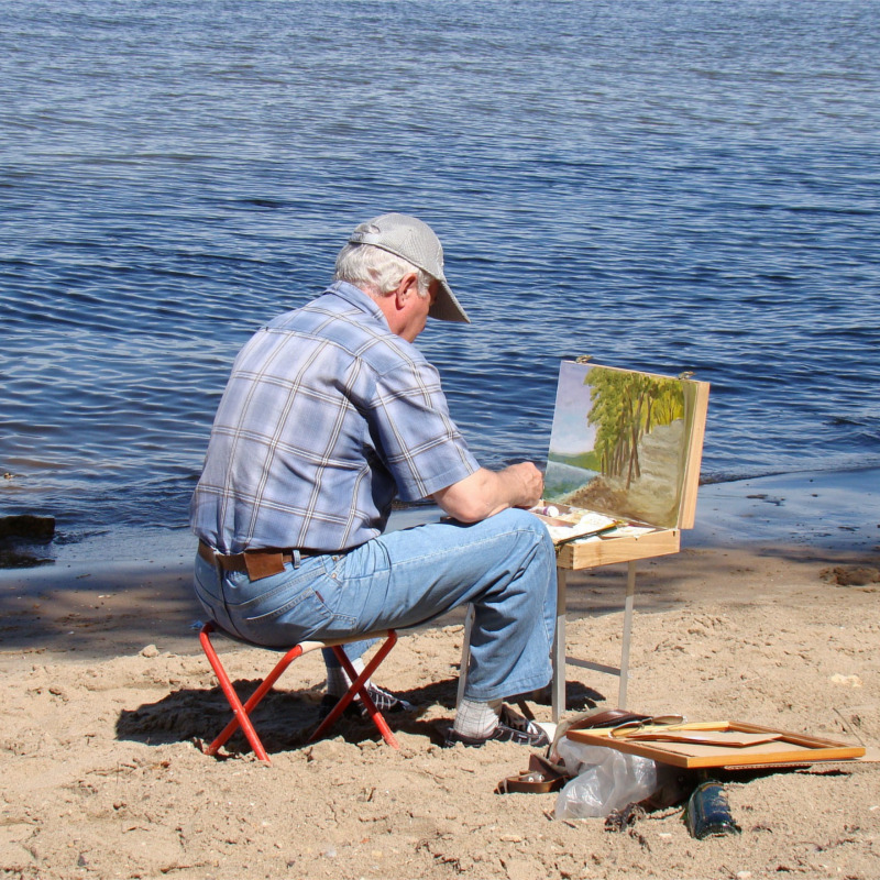 View from behind, artist painting on by seashore, ocean in background