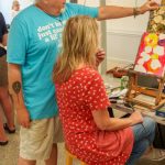 Instructor giving feedback to seated painter on circular pattern artwork.