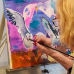 Woman painting expressive seagulls on colorful canvas with fine brush.