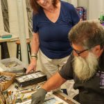 Woman observing man sketching detailed landscape in art studio.