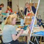 Group of women painting together in shared art classroom.