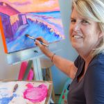 Woman painting colorful seascape on canvas at indoor easel.