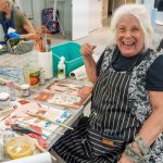 Artist laughing while working with paints at creative workspace.