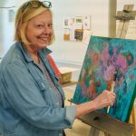 Smiling woman painting vibrant abstract artwork in art studio setting.