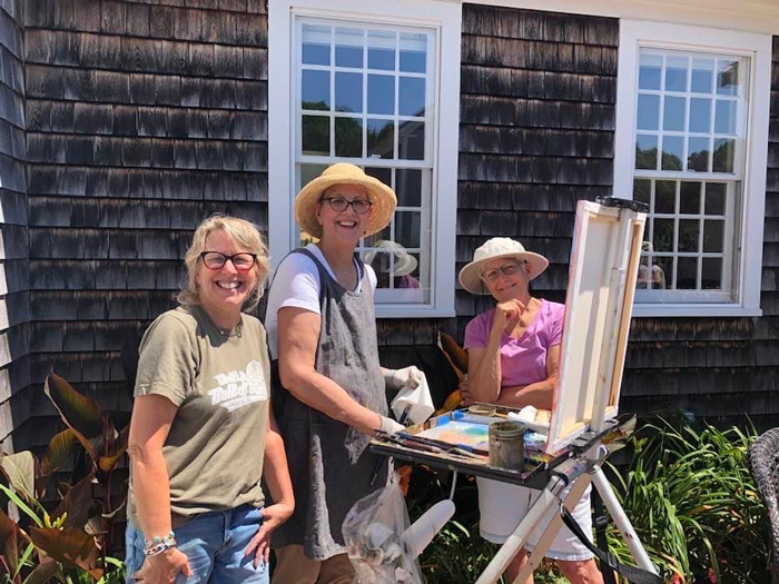 Outdoor painters smiling near easel in bright sunny yard.