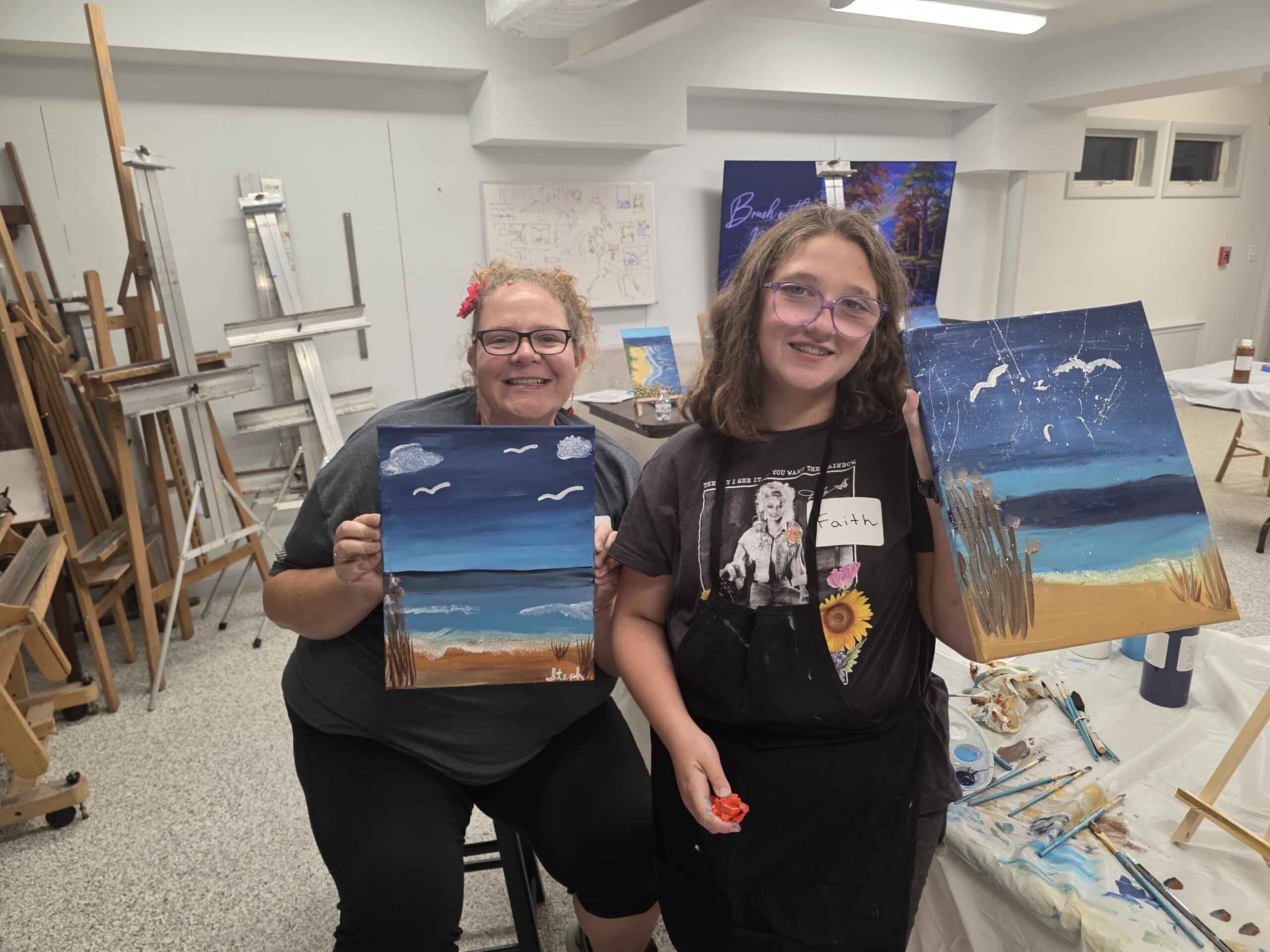 Two artists showing beach-themed paintings in studio
