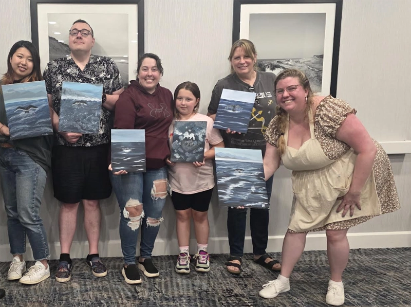 Group holding paintings, smiling indoors