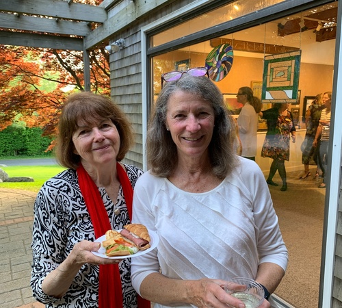 Two women smiling at gallery event with snacks and drink